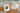 Auf einem Holztisch mit hellgrüner Tischdecke und weissen Bändern liegen zwei Hochzeitseinladungen als Klappkarten. Die linke Variante hat ein Bild der Verlobten, die rechte kommt ohne Foto nur mit Text und Cliparts aus.